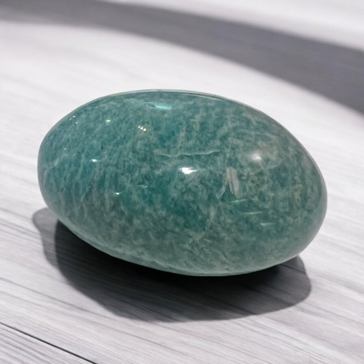 A beautifully polished Amazonite palm stone, ergonomically shaped for easy holding, showcasing calming blue-green colours and smooth textures that promote relaxation and emotional stability