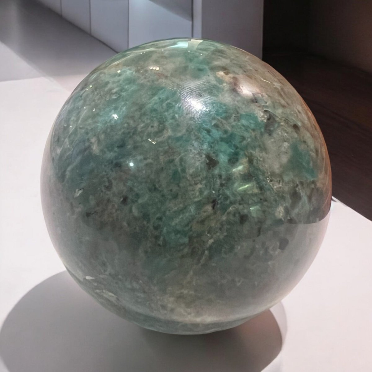 A polished crystal sphere, showcasing vibrant blue-green colours and unique natural patterns, representing unity and clarity while promoting positive energy